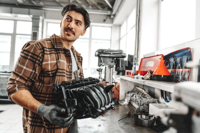 Young man mechanic repairing car parts on worktable in car service shop